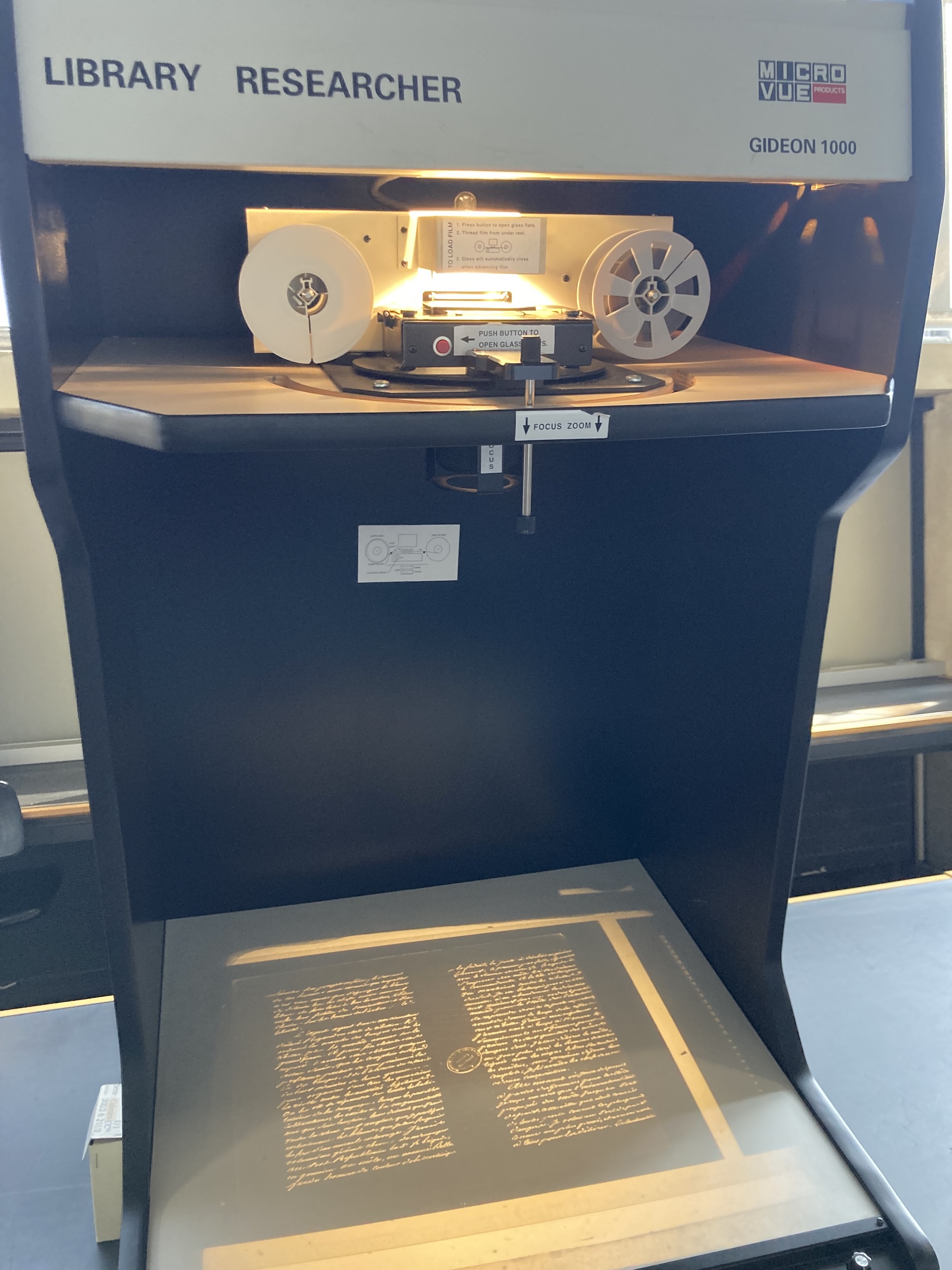 Jungki Min operating a vintage microfilm reader in a Paris archive, with the machine displaying a glowing projection of an 18th-century manuscript page.