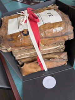 Ancient archival documents from Bordeaux, tied in bundles with white and red string, resting inside a specialized, black preservation box.