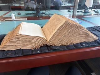 A massive, centuries-old volume of notarial records sitting open on a desk in a French archive, showing extensive historical wear on its heavy, deckled paper.