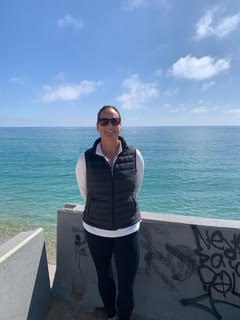 Historical researcher and doctoral candidate Victoria Sharp standing outdoors with the Mediterranean Sea and a blue sky in the background.