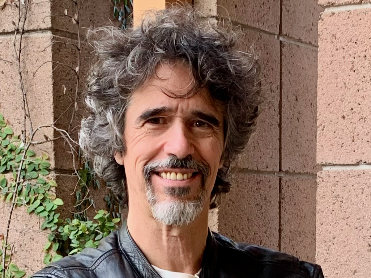 João Pedro Oliveira in a black leather jacket standing in front of a brick building.