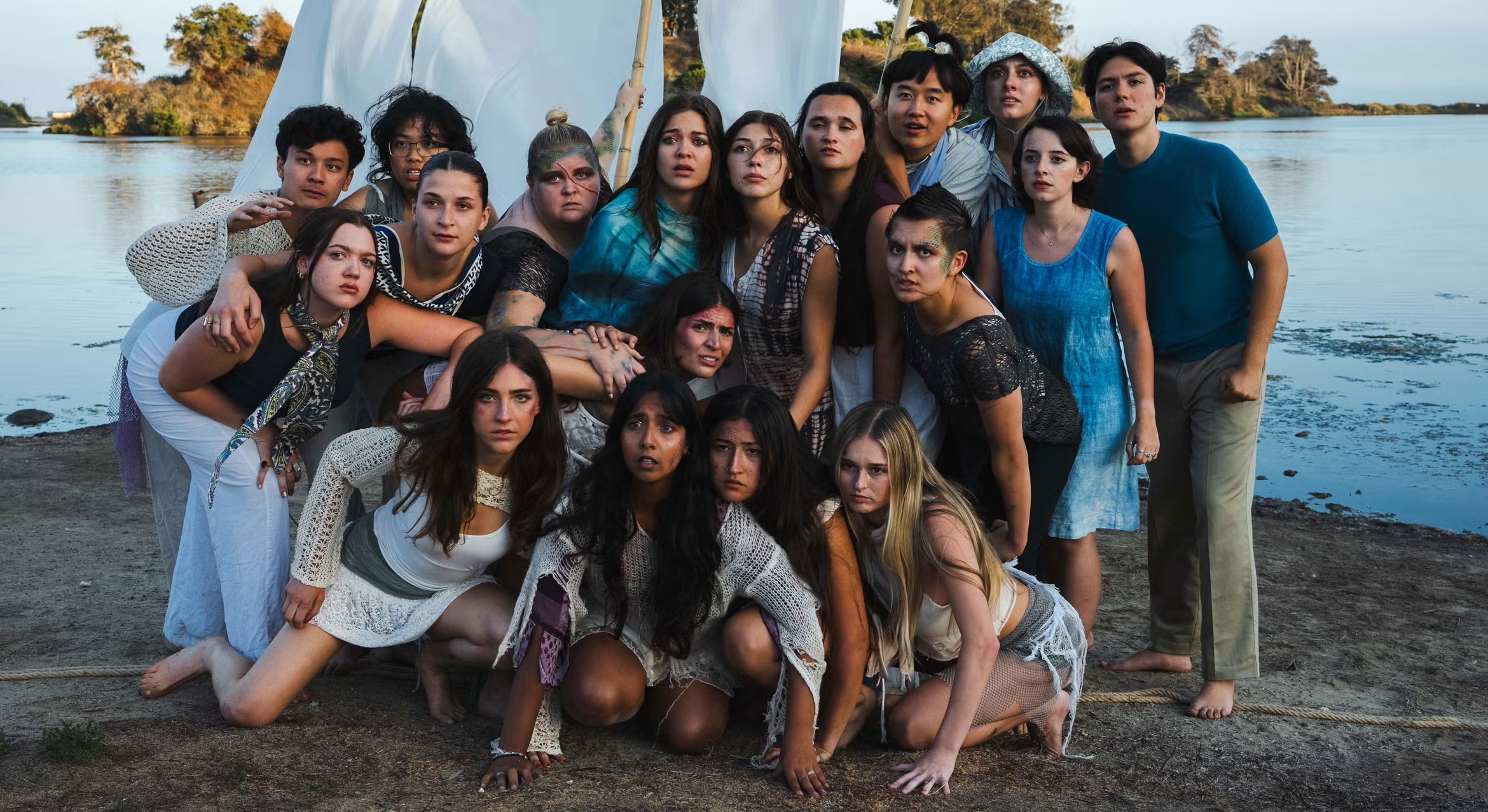The student cast of the Department of Theater and Dance's Naked Shakes production of "The Tempest" poses together as a group on a beach at sunset.