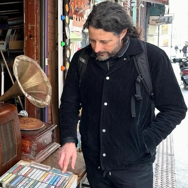 David Novak looks through a display box of cassette tapes outside a brick music shop in Istanbul. A vintage radio and gramophone sit nearby.