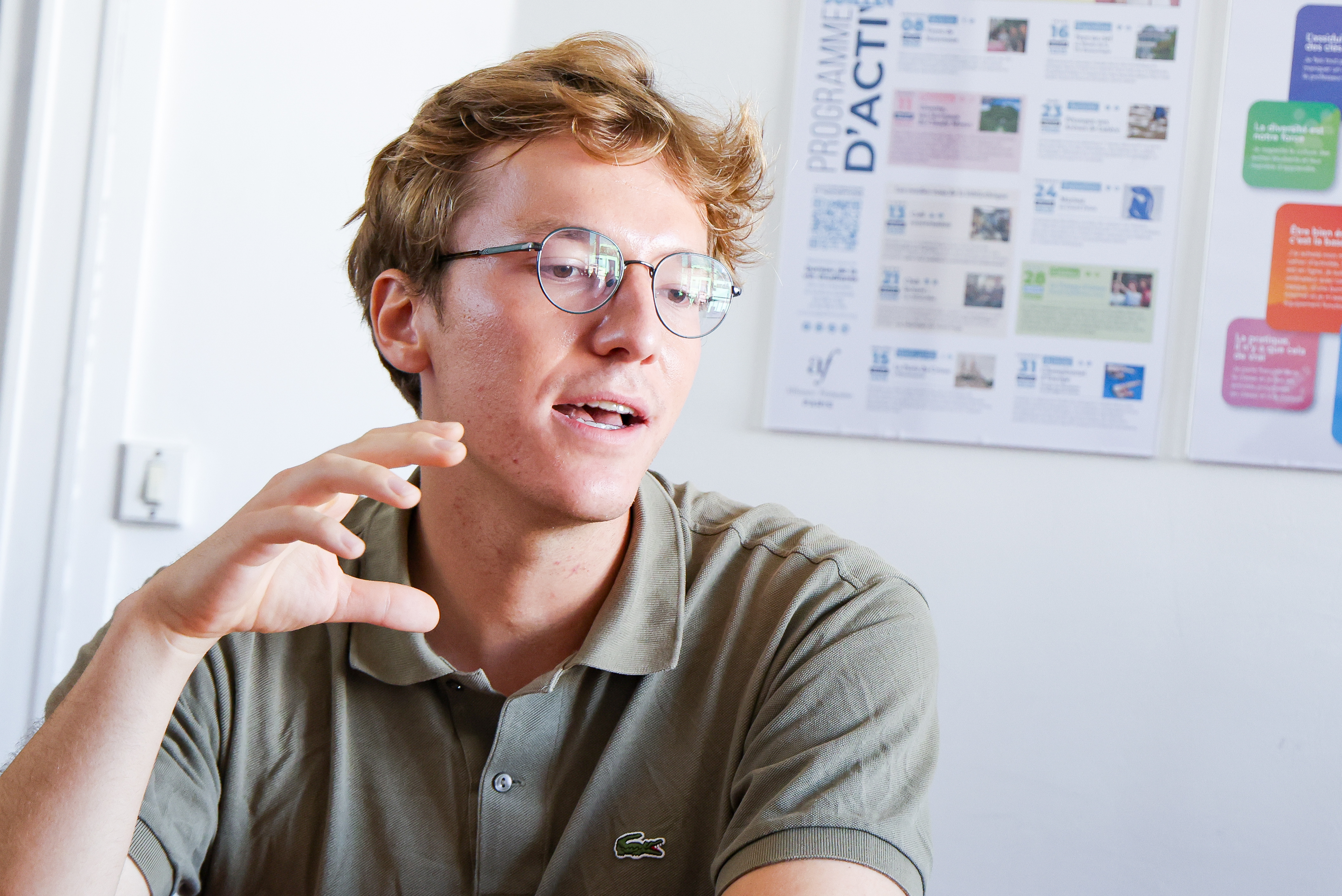 Matthieu Huy, wearing a green polo shirt and wire-rimmed glasses, gestures with his right hand while speaking.