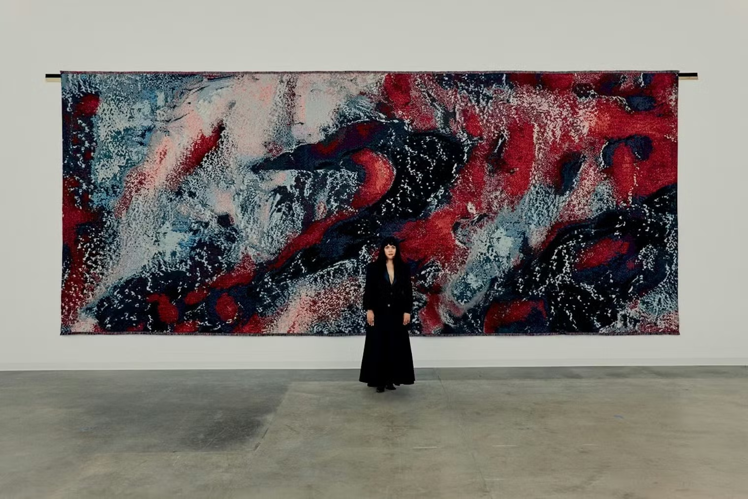 Artist Sarah Rosalena stands before a large red, blue, white and black textile work in LACMA’s David Geffen Galleries.